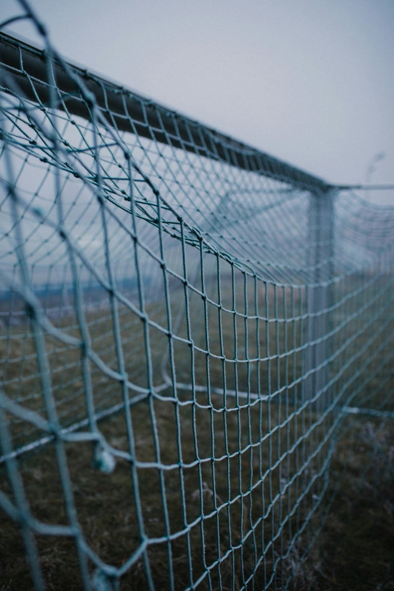 A soccer net stands in a foggy landscape, partially obscured by mist, creating a mysterious atmosphere.